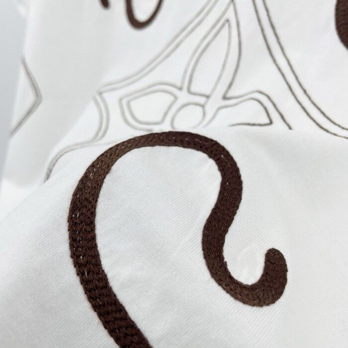 Tessuto bianco con ricami floreali marroni eleganti e dettagli raffinati, perfetto per arredi sofisticati.