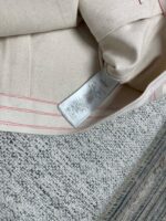 Tessuto beige con linee rosse e etichetta di cura, su sfondo da tappeto grigio.