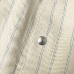 Tessuto beige con righe blu e bottone metallico elegante, ideale per moda e arredamento.