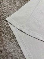 T-shirt in cotone leggero con cuciture precise, su sfondo testurizzato naturale e elegante.