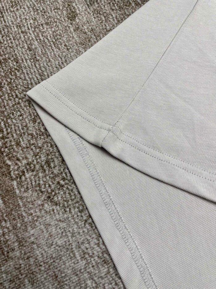 T-shirt in cotone leggero con cuciture precise, su sfondo testurizzato naturale e elegante.