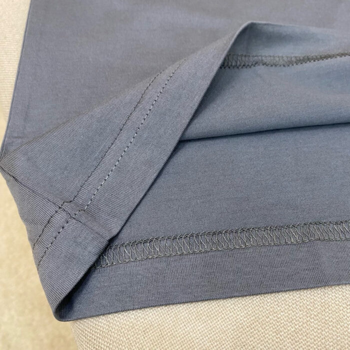 Dettaglio dellorlo ricurvo di una camicia in cotone grigia con cuciture precise e stile elegante.