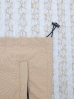 Borsa in nylon beige con coulisse e chiusura a toggle, su sfondo testurizzato.