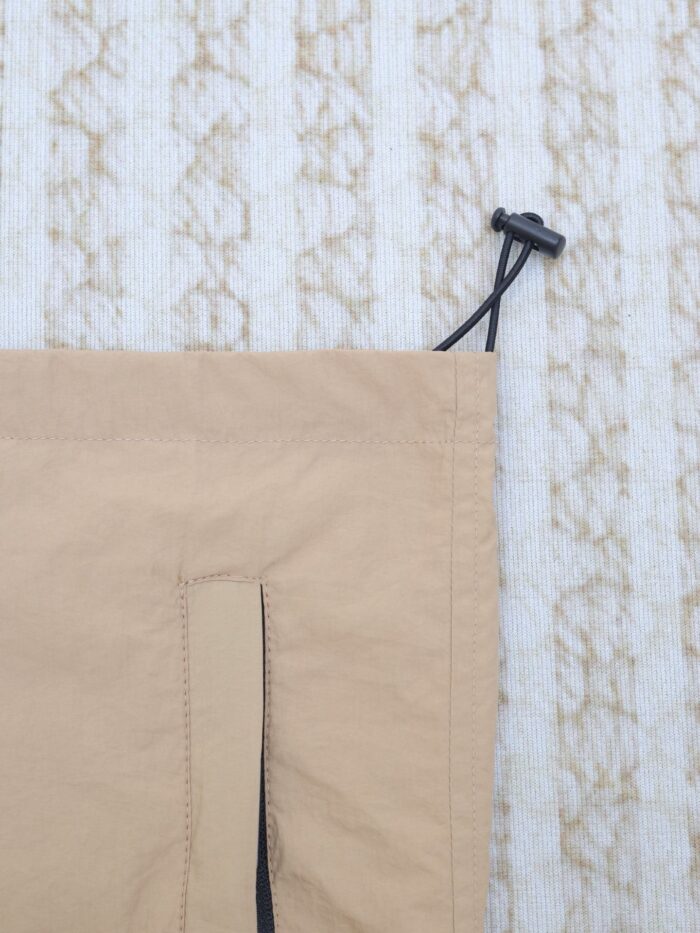 Borsa in nylon beige con coulisse e chiusura a toggle, su sfondo testurizzato.