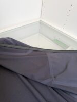 Tessuto scuro su vetro in ambiente minimalista, dettagli di texture e riflessi di luce.
