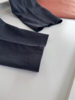 Tessuti eleganti contrastanti: tweed scuro e lino pesca su sfondo bianco minimalista.