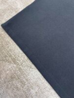 Contrasto tra tessuto scuro e superficie chiara, texture morbida e raffinata, dettaglio sartoriale e casa.