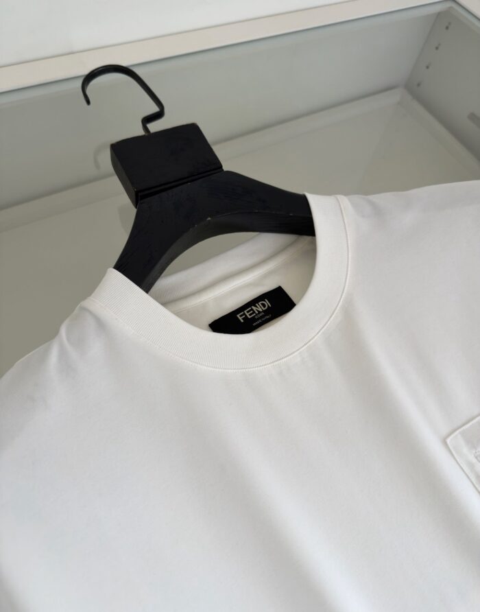 Maglietta bianca Fendi con logo elegante e design minimalista, esposta su appendino nero di alta qualità.