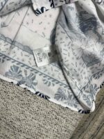 Tessuto con motivo floreale blu, etichetta cura, dettaglio artigianale, perfetto per abbigliamento e decorazione.