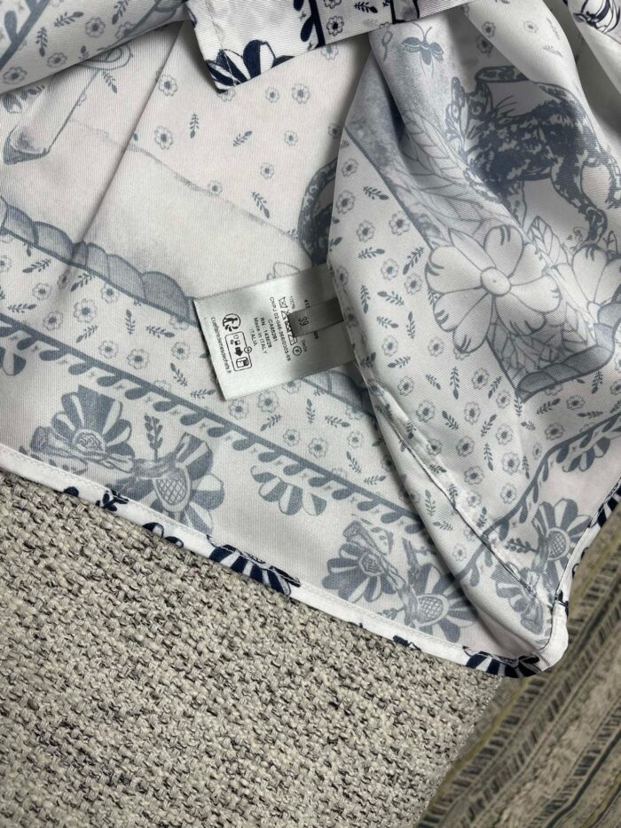Tessuto con motivo floreale blu, etichetta cura, dettaglio artigianale, perfetto per abbigliamento e decorazione.