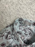 Dettaglio del colletto di camicia Dior con motivo floreale su sfondo azzurro pastello.