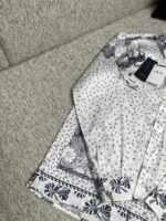 Camicia bianca con motivi floreali delicati su divano chiaro, elegante e casual.