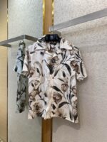 Camicia estiva floreale maniche corte in tessuto leggero su sfondo beige, stile naturale ed elegante.