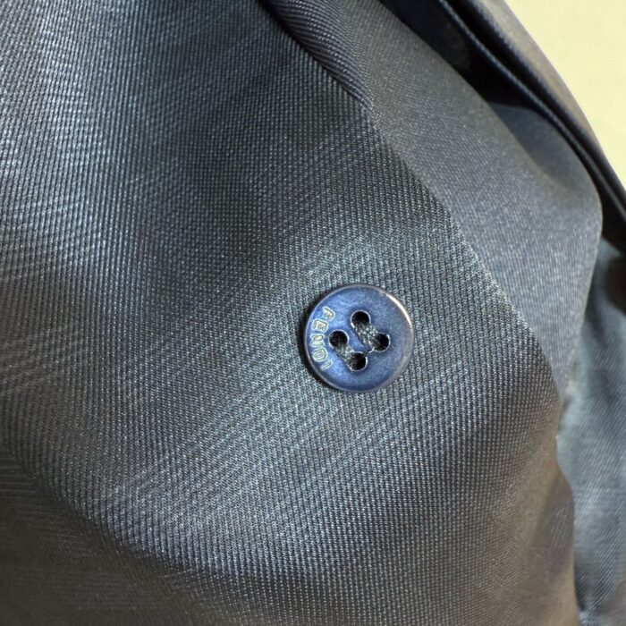 Dettaglio di bottone elegante su giacca da uomo in tessuto scuro e raffinato.