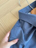 Camicia blu elegante appesa, dettaglio di mano con smalto, stile e cura del guardaroba.