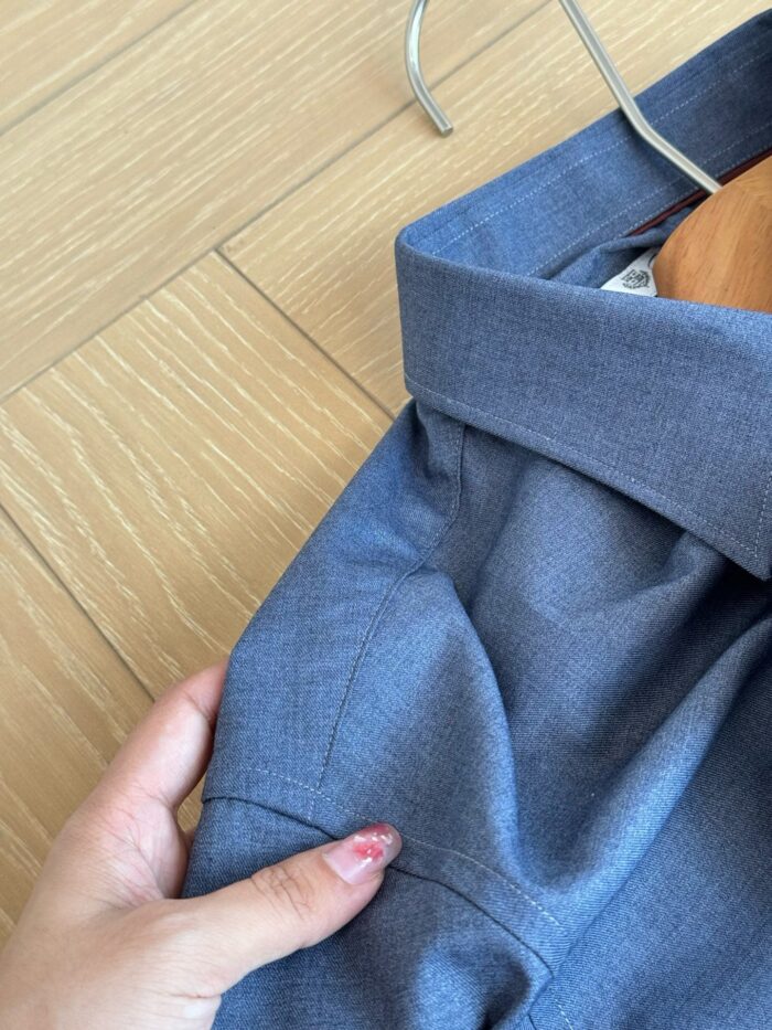 Camicia blu elegante appesa, dettaglio di mano con smalto, stile e cura del guardaroba.