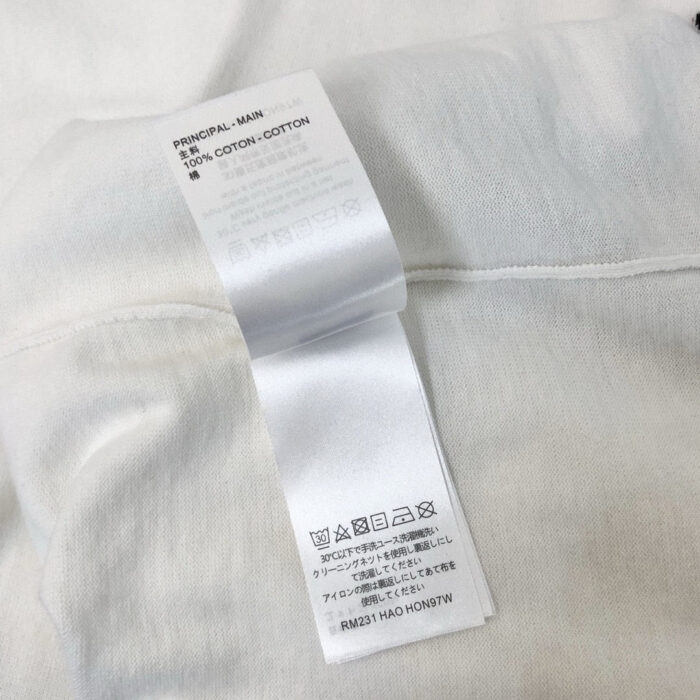 Maglietta bianca in cotone con etichetta di cura e comfort, vestibilità semplice e leggera.
