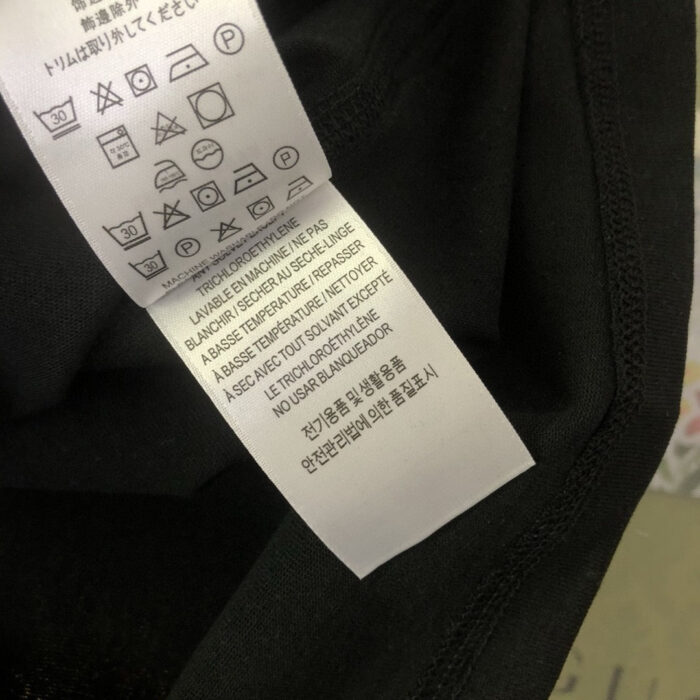 Etichetta di cura vestiti con simboli e istruzioni multilingue per il lavaggio e lasciugatura.