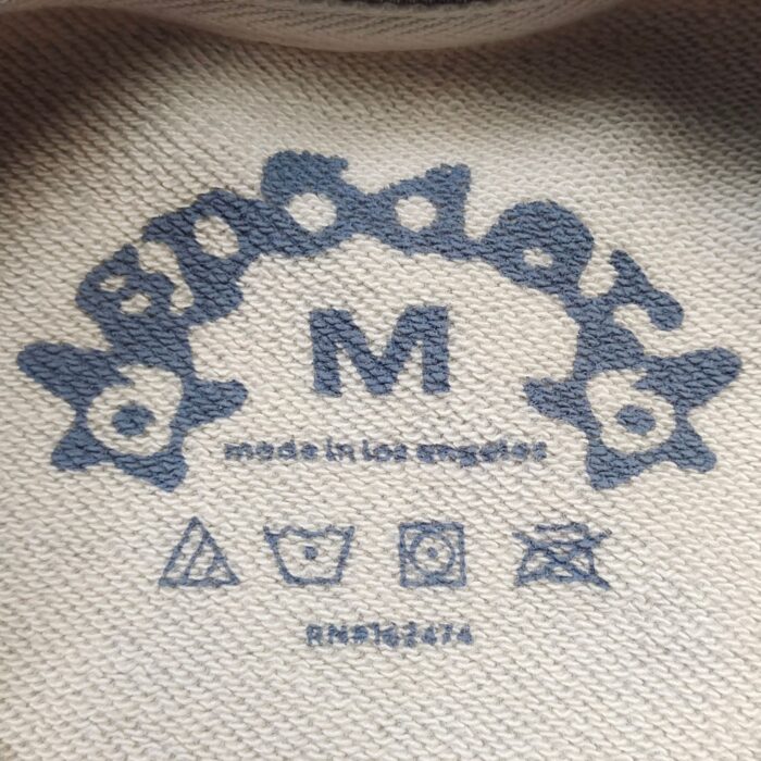 Etichetta abbigliamento Made in Los Angeles con simboli cura e design blu suggestivo.