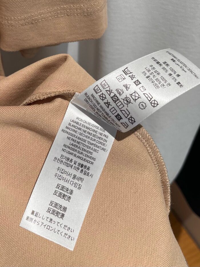 Etichetta di cura tessile con simboli per lavaggio e istruzioni multilingue su abbigliamento beige.
