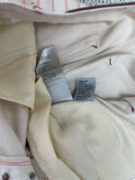 Interno di giacca con etichette di cura, cuciture rosse e tessuto morbido color crema.