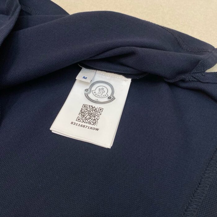 Etichetta interna in tessuto navy con logo, taglia M e QR code, dettaglio di qualità.