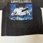 Maglietta nero Ghost in the Shell con protagonista cyberpunk, skyline futuristico e testo bianco.