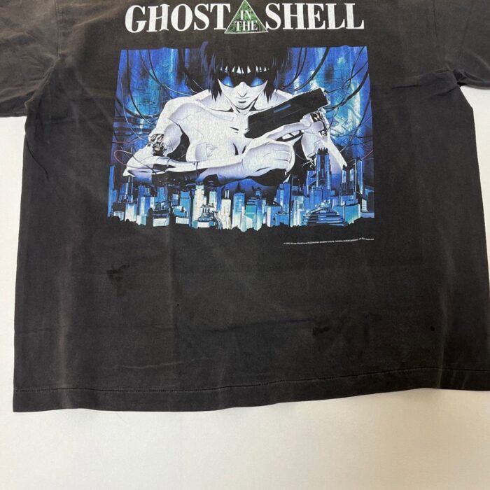 Maglietta nero Ghost in the Shell con protagonista cyberpunk, skyline futuristico e testo bianco.