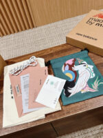 Set regalo con borsa teal, dettagli informativi e scatola New Balance su superficie in legno.