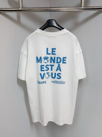 Maglietta bianca con messaggio ispiratore Le Monde Est À Vous e globi, ideale per uno stile positivo.