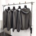 Lotta di 4 felpe grigie con cappuccio su esposizione minimalista in boutique elegante.