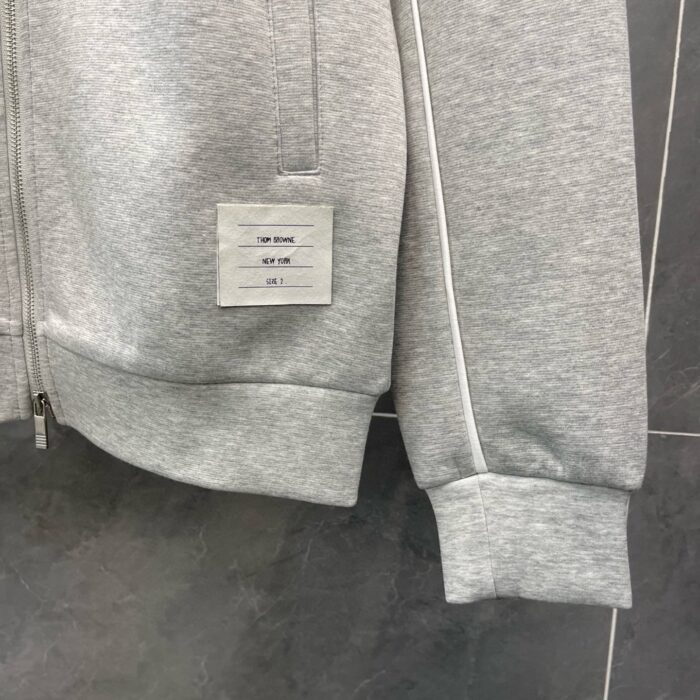 Felpa grigia minimalista con zip, etichetta davanti e dettagli comodi, stile urbano e casual.