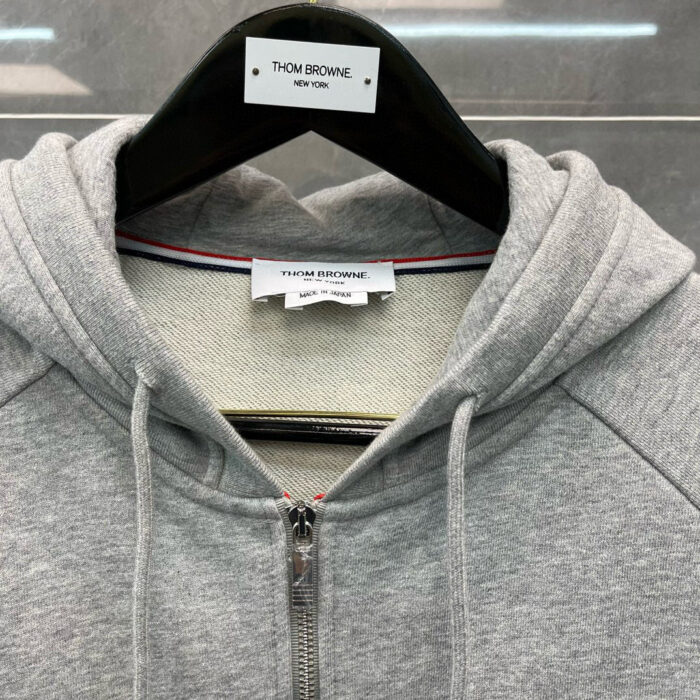 Felpa grigia Thom Browne con zip, interno a strisce e logo di alta qualità.