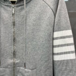 Felpa grigia con zip, cappuccio regolabile e strisce sportive bianche sul braccio.