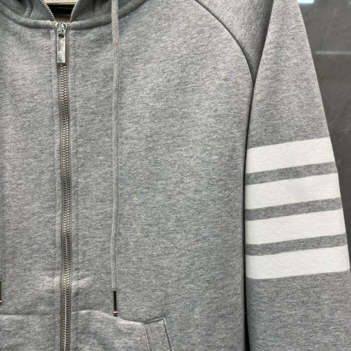 Felpa grigia con zip, cappuccio regolabile e strisce sportive bianche sul braccio.