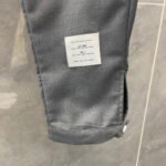 Pantaloni grigi eleganti con dettaglio a polsino, etichetta e tessuto lucido.