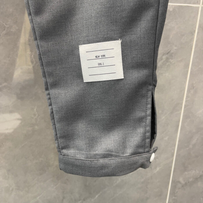 Pantaloni grigi eleganti con dettaglio a polsino, etichetta e tessuto lucido.