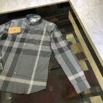 Camicia casual check grigia nuova su tavolo in vetro, stile moderno e comfort.