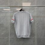 Maglione grigio corto con strisce rosse sulle maniche, stile sportivo e moderno.