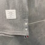 Camicia grigia con bottoni bianchi e dettaglio a righe rosse, bianche e blu sullorlo.