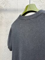 Maglietta grigia casual con scollo rotondo e dettagli morbidi, su appendiabiti verde.