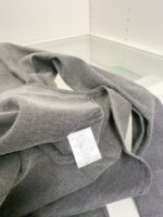 Maglione grigio morbido con etichetta di cura, stile casual e comfort elegante.