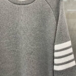 Maglione grigio sportivo con collo rotondo e strisce bianche sulle maniche.