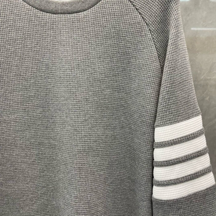 Maglione grigio sportivo con collo rotondo e strisce bianche sulle maniche.