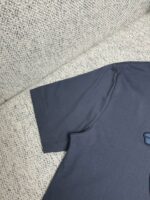 Dettaglio manica di una t-shirt grigia casual su sfondo tessuto neutro.