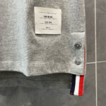 Maglietta grigia sportiva con bottoni metallici, fascia colorata e etichetta minimalista TROY BROWN.