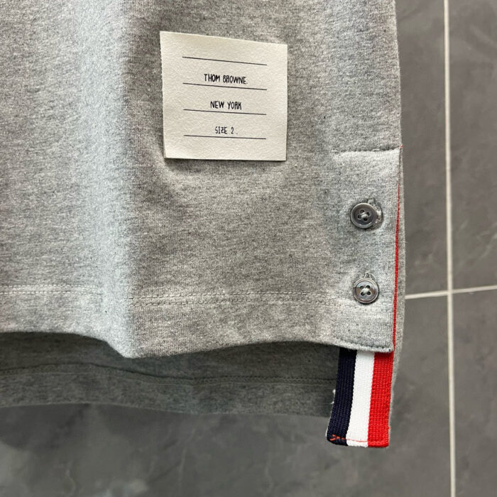 Maglietta grigia sportiva con bottoni metallici, fascia colorata e etichetta minimalista TROY BROWN.