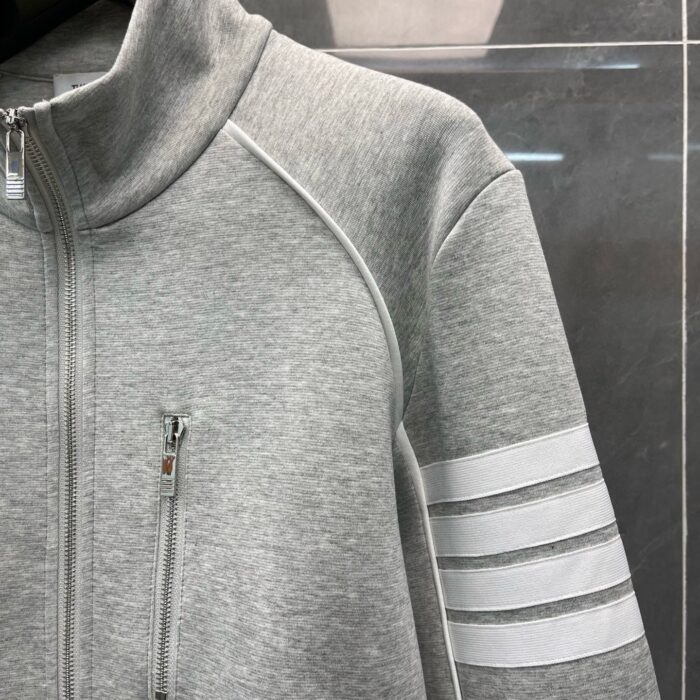 Giacca sportiva grigia con strisce bianche, zip e collo alto, ideale per fitness e casual.