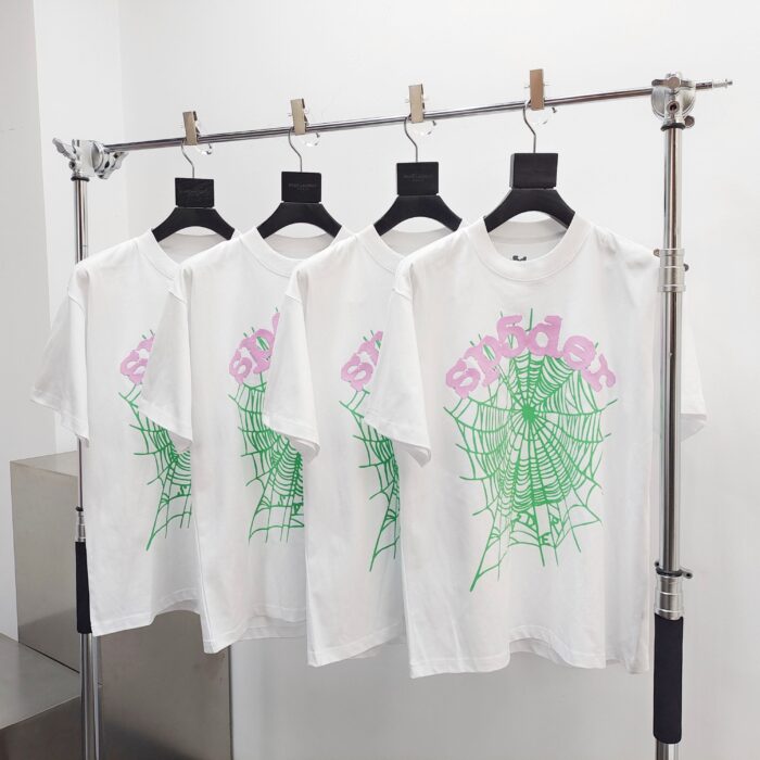 Magliette bianche con grafica di ragno verde e testo rosa, stile trendy e giovane.