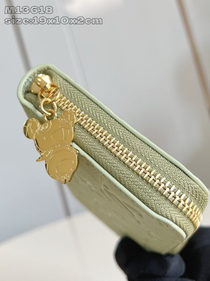 Portafoglio verde elegante con cerniera dorata e charm giocoso, ideale per ogni occasione.